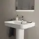 Waschtisch von Ideal Standard mit klaren Kanten, integriertem Wasserhahn und Ablagefläche, montiert auf einer weißen Säule in einem modernen Badezimmer.